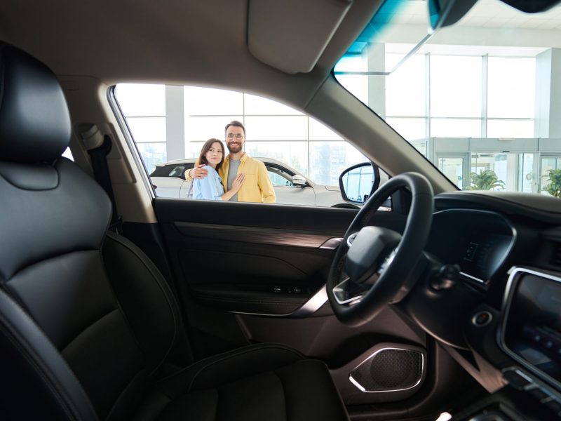 Photo of car interior with loving couple posing at camera in background in car showroom